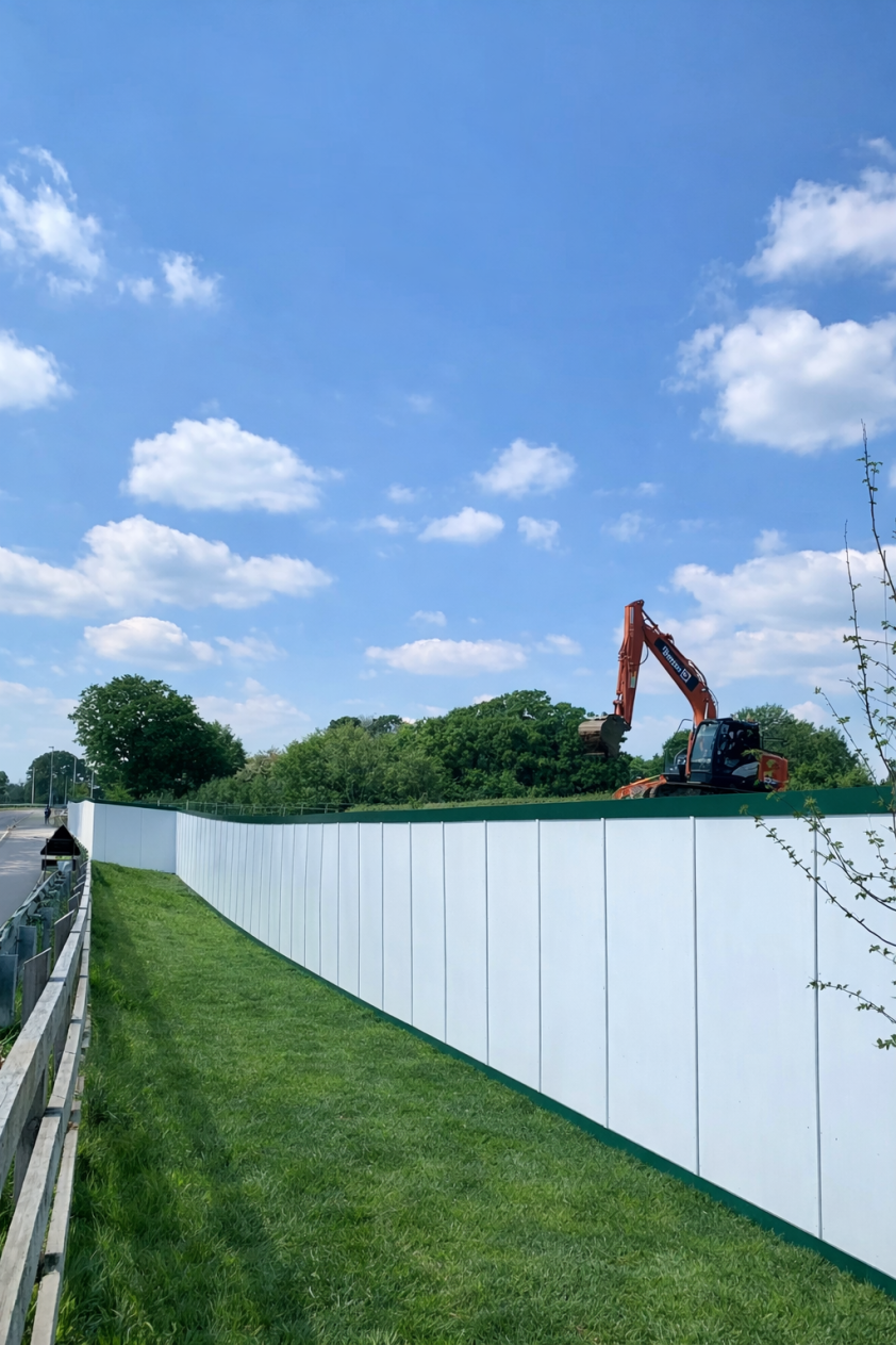 White site hoarding with green trim along a road