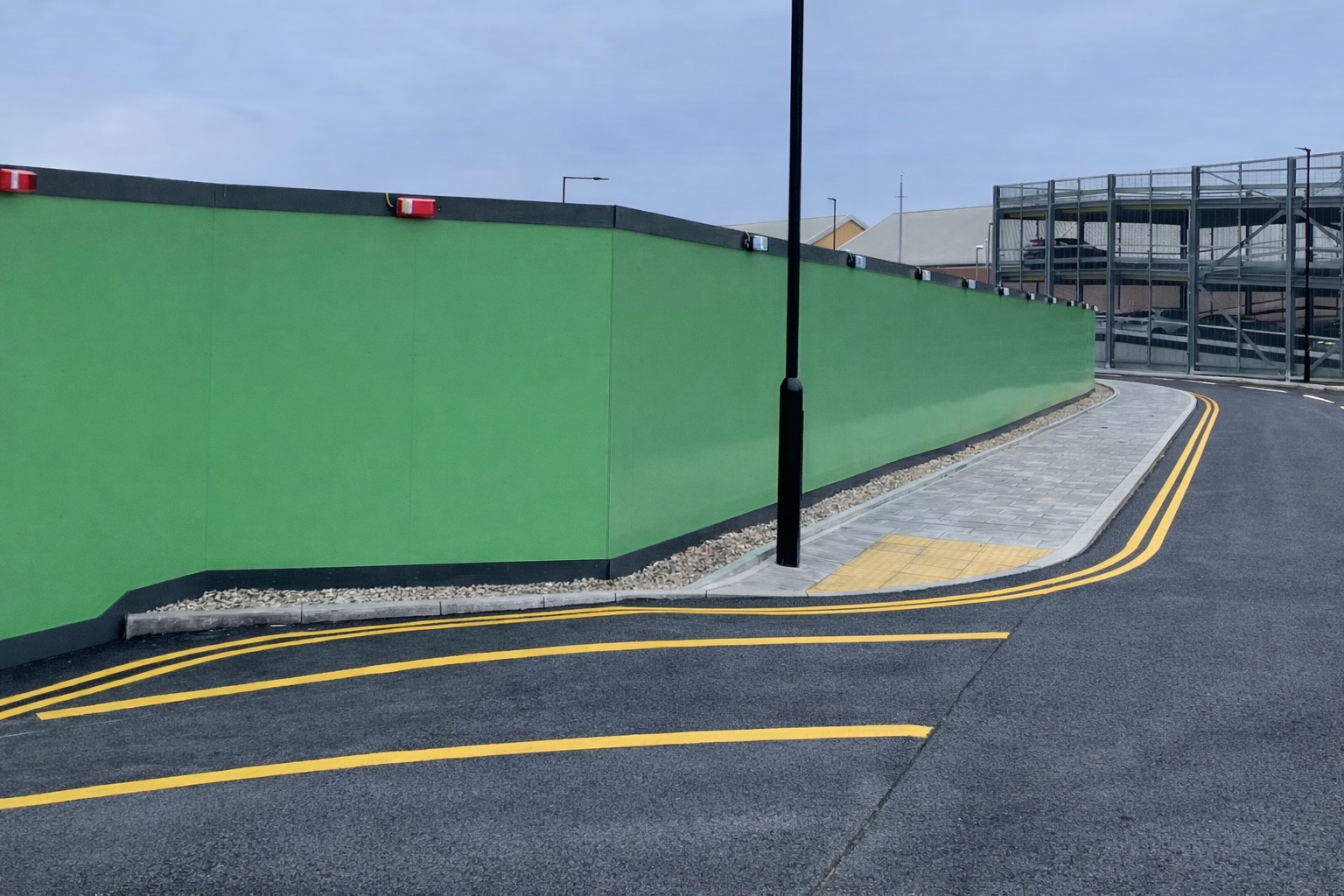 Green painted construction site hoarding along a curved road